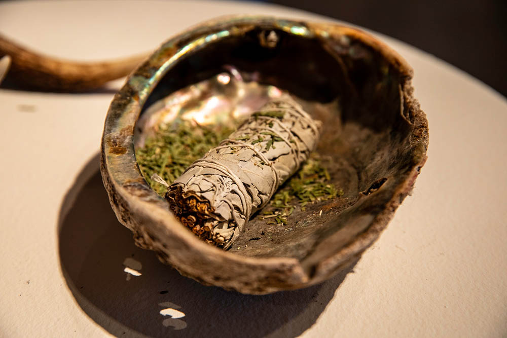 A close of a abalone bowl with a smudge stick inside.